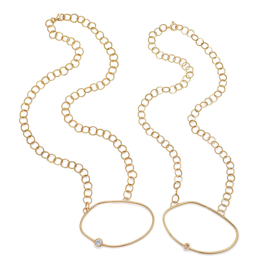 Two cell necklaces side by side – both yellow gold necklaces with an asymmetric oval pendant, one with a champagne diamond off the centre and the other with a white diamond - inspired by a cell.
