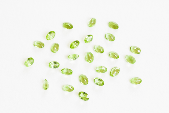A collection of bright green peridot precious gems, scattered on a white background.